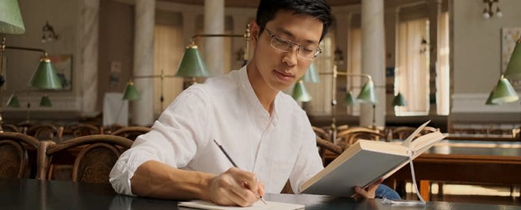 A Man Reading A Book While Taking Down Notes